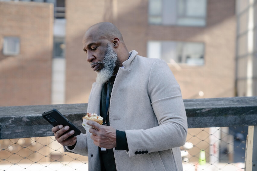 man walking while eating a sandwich and holding phone reading about tax tips