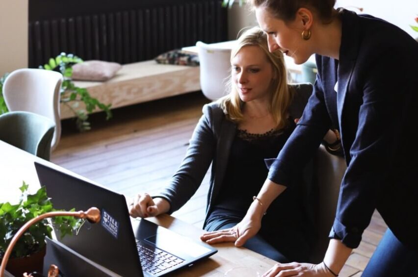 smiling colleagues looking at laptop in office