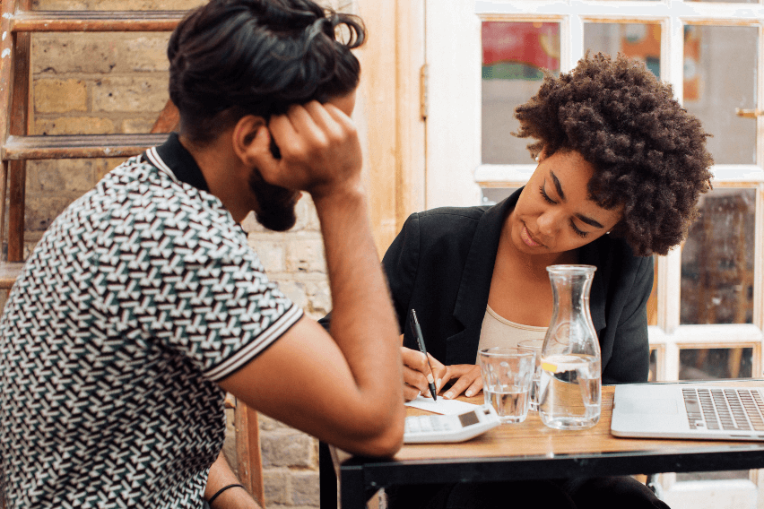 Man and woman sitting at cafe table looking at paper woman is writing on