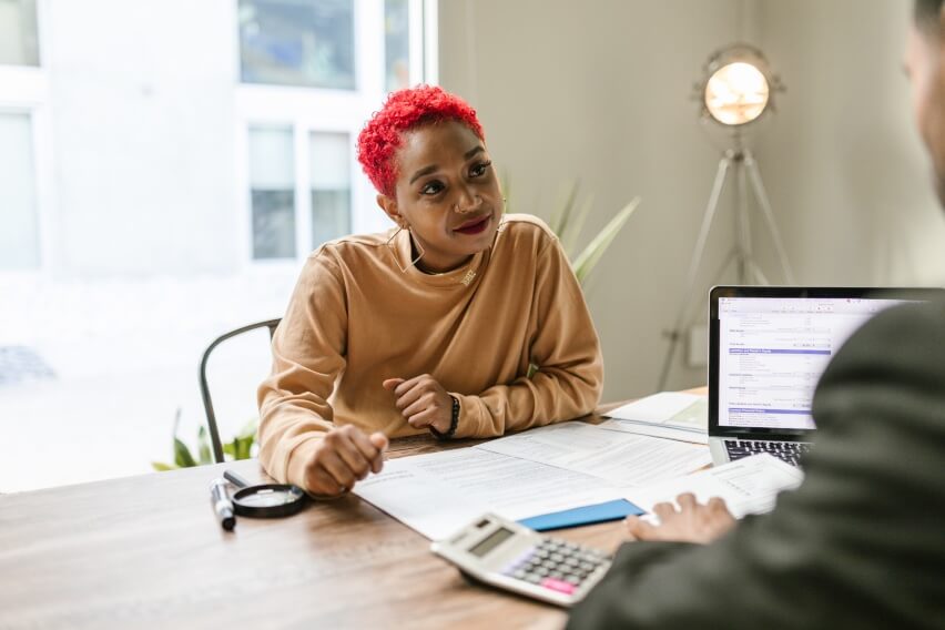 seated smiling person at work, looking at another person across table