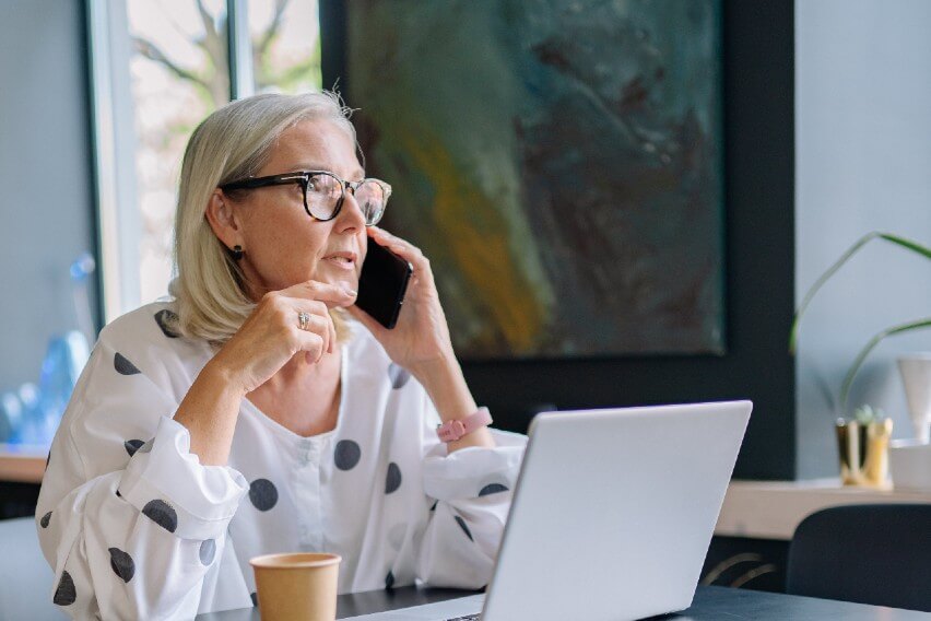 woman talking on phone in cafe with laptop on table